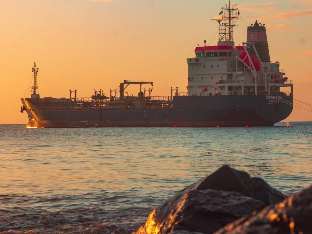 Large oil tanker on the ocean near the coast, sailing under a vibrant sunset sky.