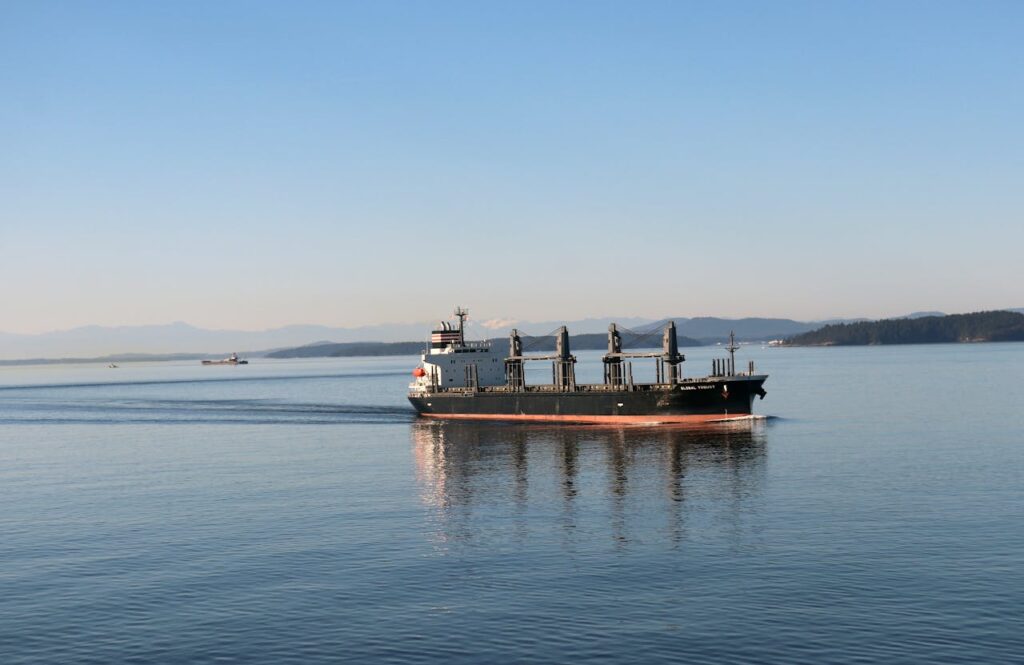 Cargo ship cruising through calm waters with distant mountains in view, during daytime.